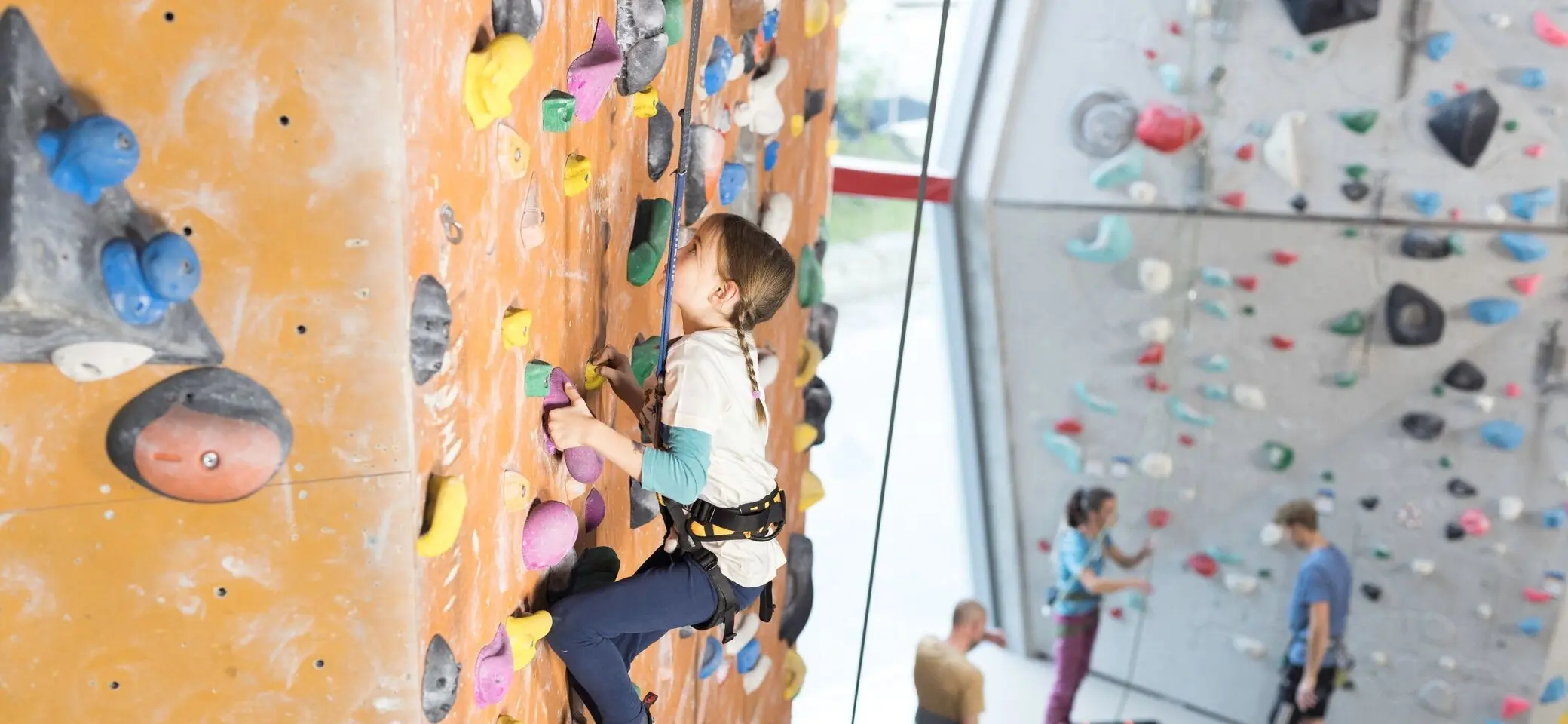 Ein Mädchen beim Familienklettern in der Kletterhalle des DAV. Im Hintergrund weitere Kletterer | © DAV / Jens Klatt